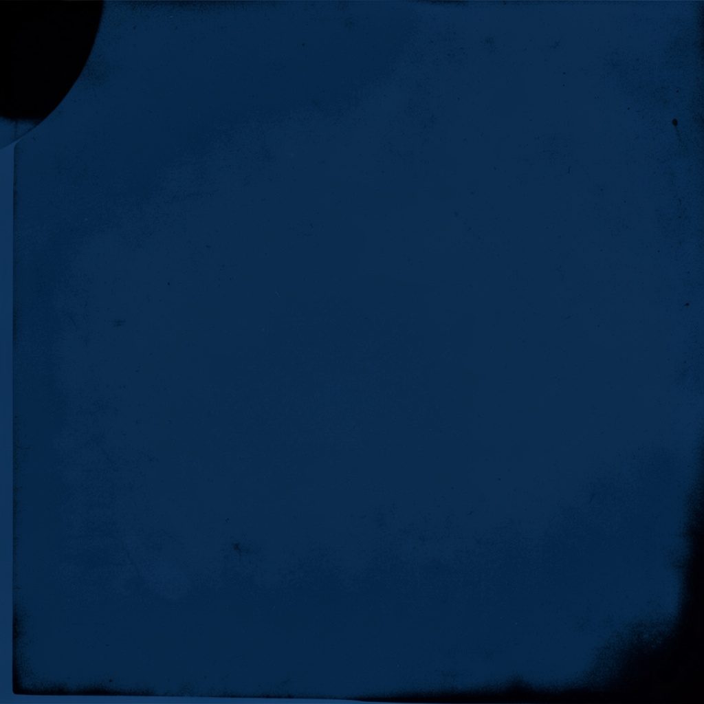 A duotone photograph in deep navy blue and warm tan tones showing an open Bible resting on a wooden surface, casting long soft shadows in a quiet study